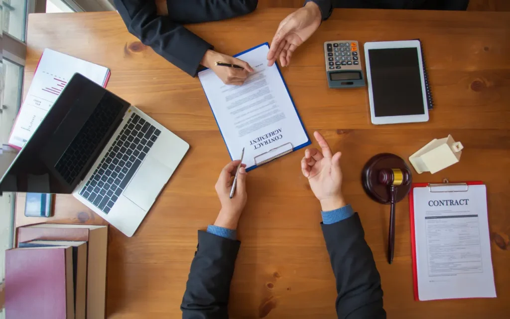 visão de cima de pessoas reunidas em uma mesa apontando e assinando um contrato, fazendo referência à uma contratação de um serviço protegido pelo seguro de responsabilidade civil