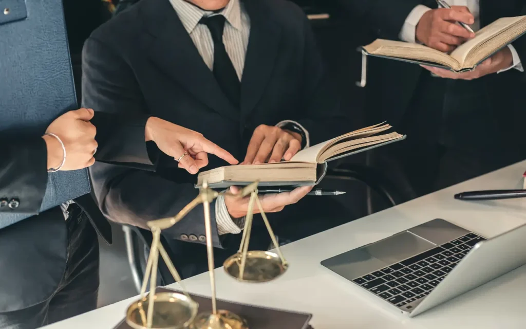 Advogados trabalhando em conjunto na frente de um notebook enquanto apontam para um livro