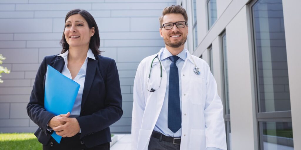 Imagem de uma advogada e um médico, ambos sorrindo, andando lado a lado em frente a um prédio moderno