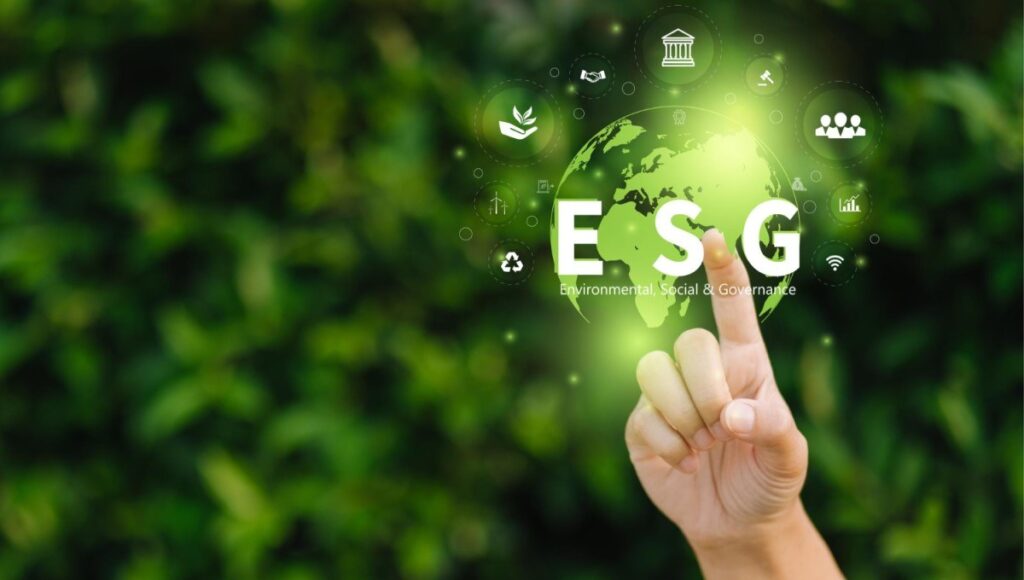 Dedo apontando para ícones digitais de ESG (Environmental, Social, and Governance) projetados sobre um globo holográfico verde, com fundo de folhagem, simbolizando sustentabilidade e práticas empresariais responsáveis.