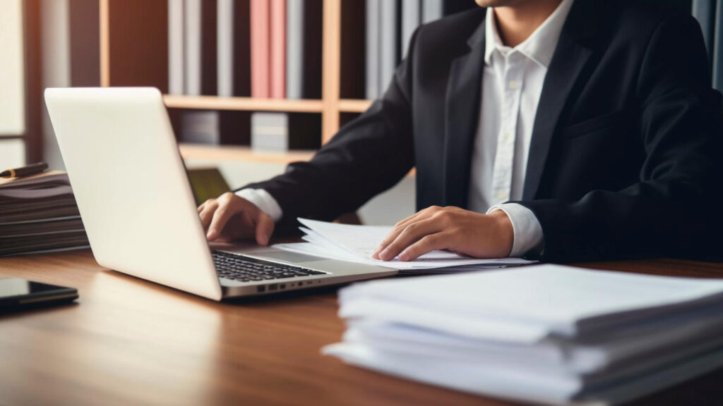 Advogado trabalhando com laptop e documentos em uma mesa.