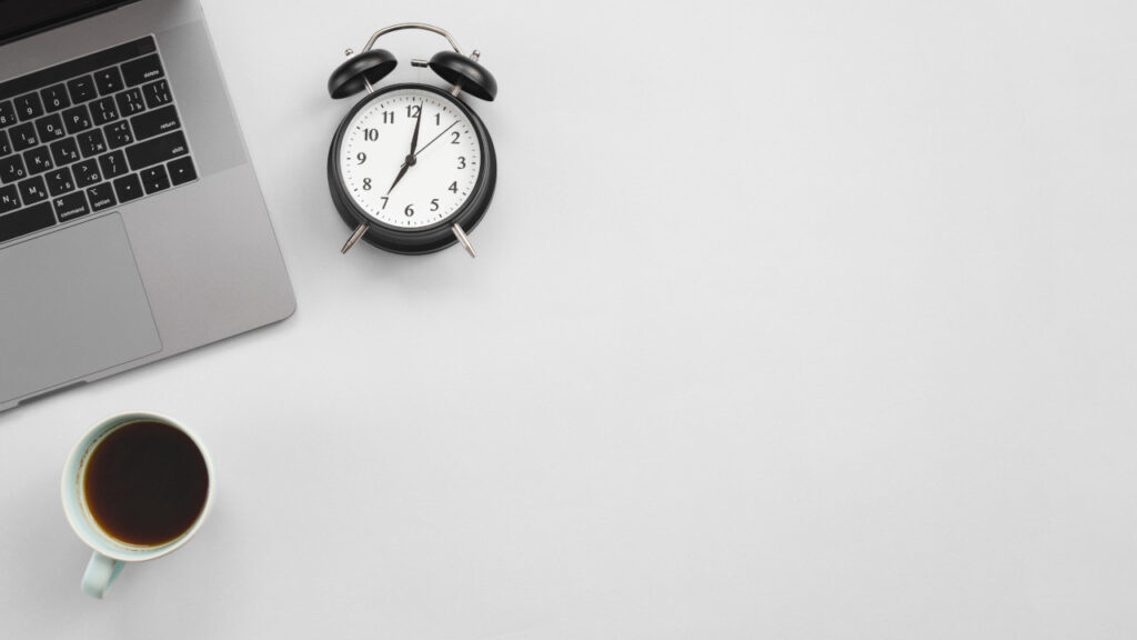 Mesa de trabalho com um laptop, um relógio analógico e uma xícara de café.