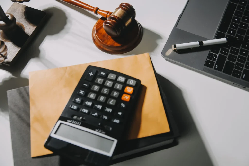 Imagem de uma mesa de escritório com calculadora, laptop, gavel de juiz, caneta e papel, representando temas de direito, advocacia e matemática.