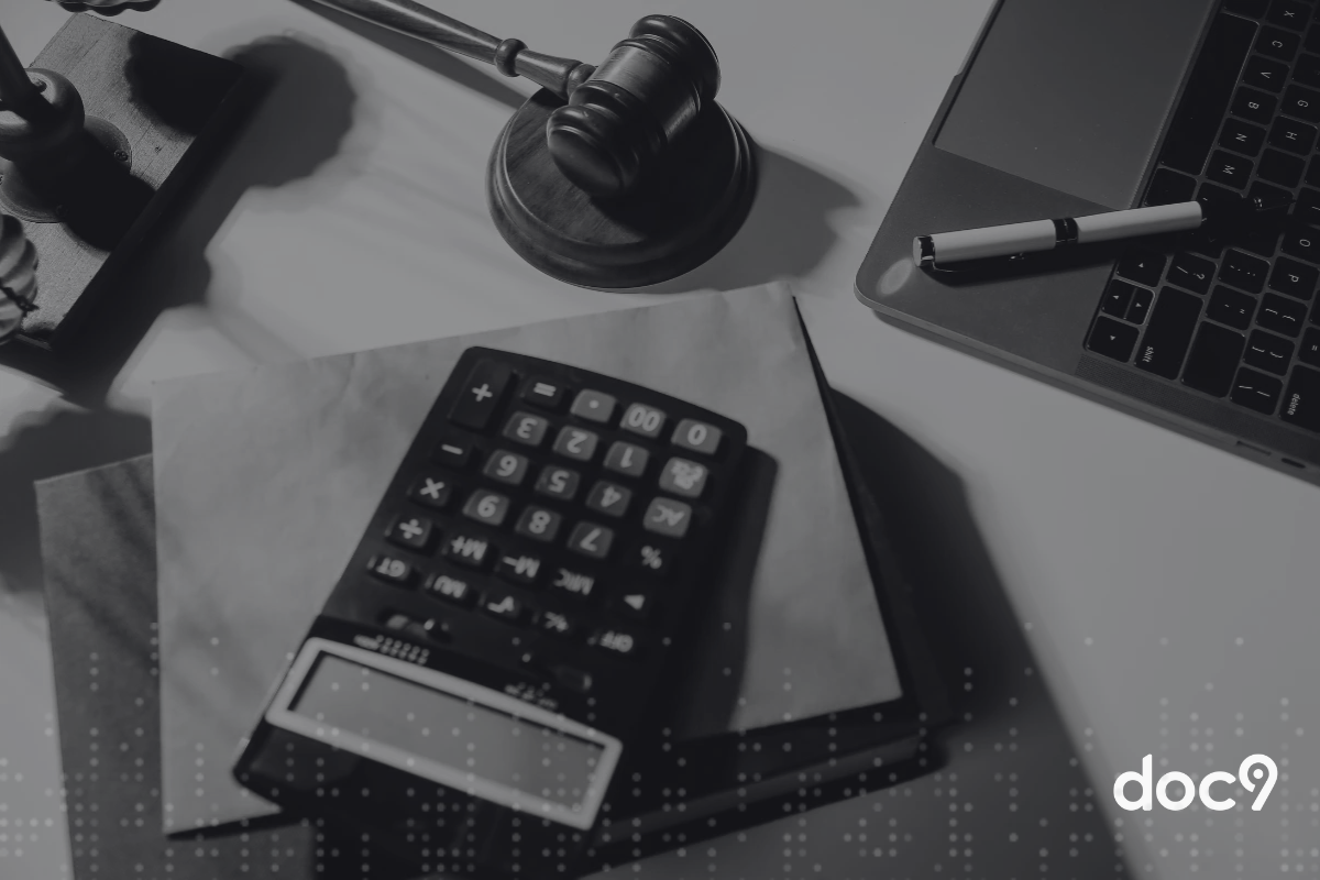 Imagem de uma mesa de escritório com uma calculadora, laptop, gavel de juiz, caneta e papel, representando temas de direito, advocacia e matemática.