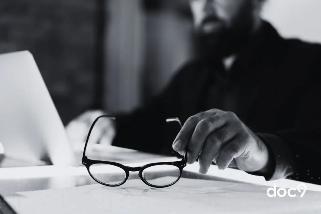 Imagem empreto e branco de um homem segurando um óculos de grau com a mão esquerda, enquanto lê um documento, representando um artigo sobre advocacia moderna em 2026 da doc9.