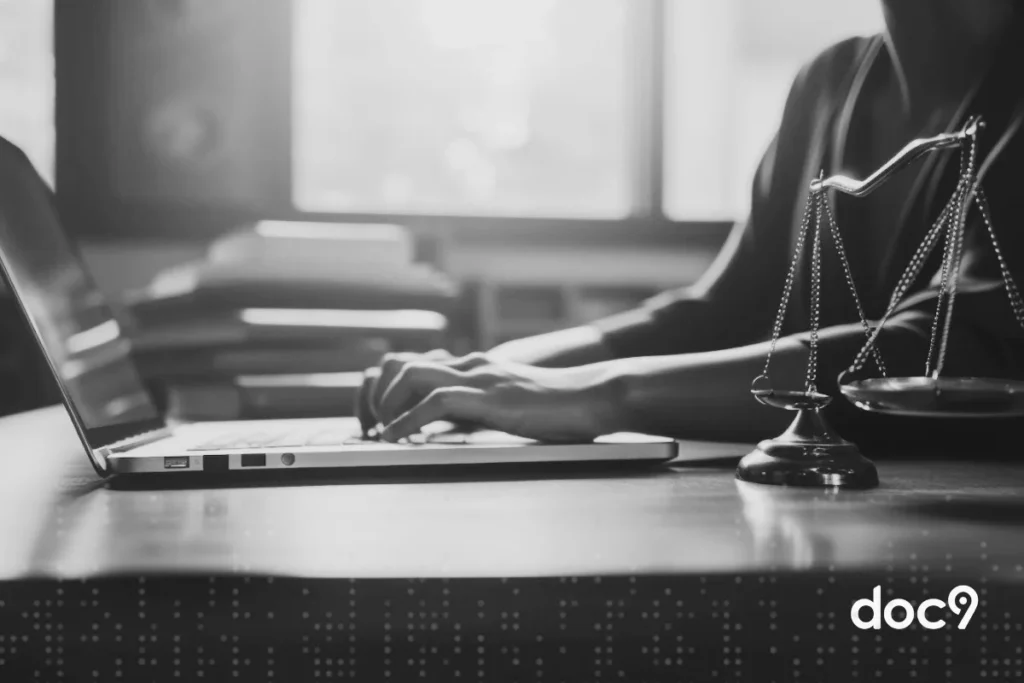 Mãos digitam em um teclado de notebook que está sobre uma mesa, com um símbolo da advocacia ao lado, representando um artigo da doc9 tudo sobre compliance jurídico.