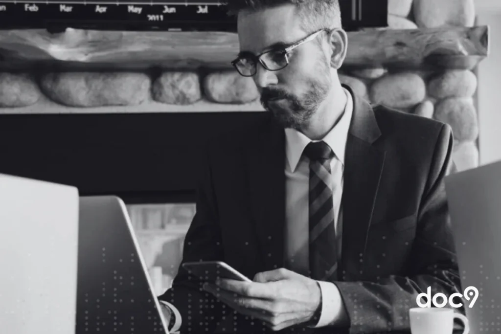 Advogado digita em teclado de notebook apoiado sobre uma mesa, enquanto segura um celular com a outra mão, representando um correspondente jurídico da doc9.