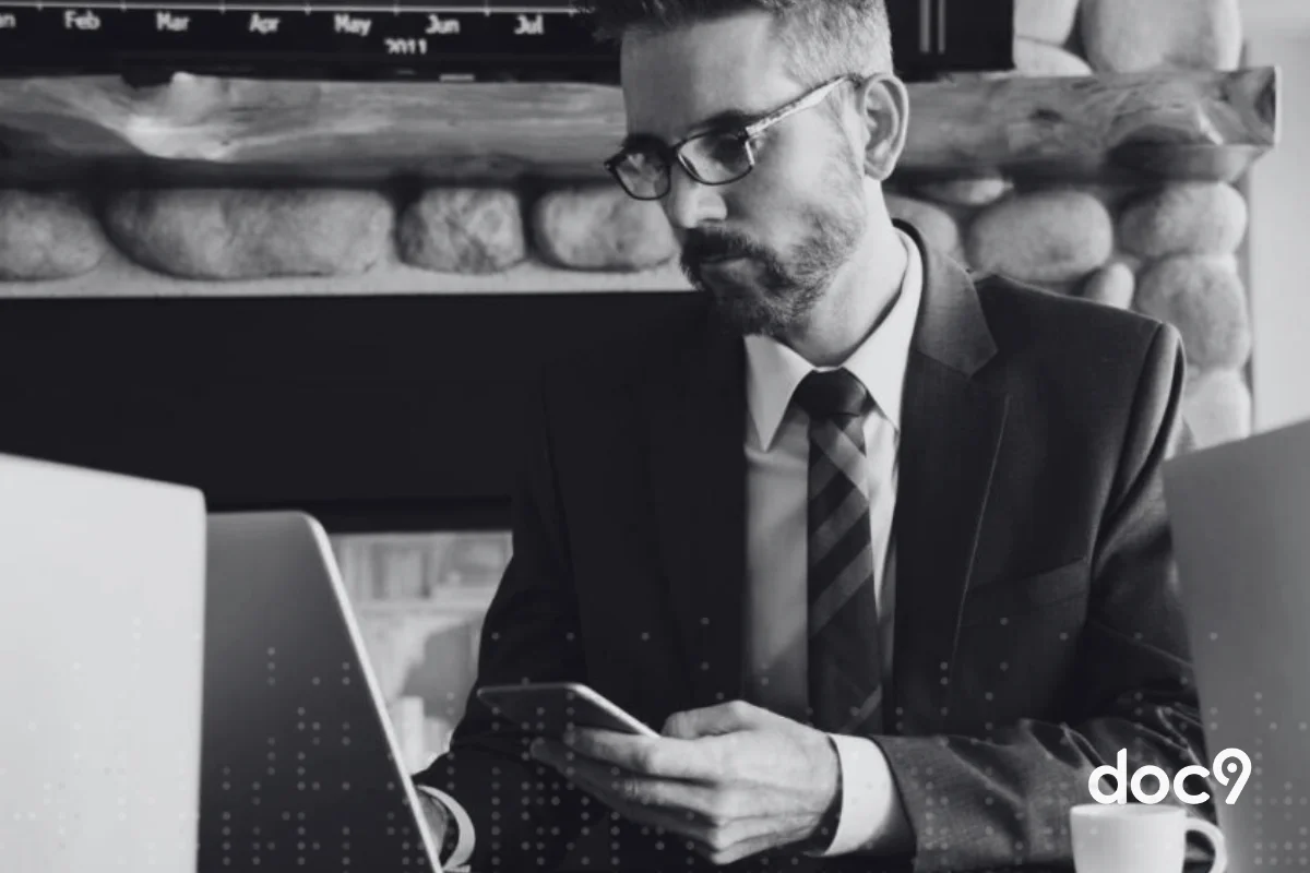 Advogado digita em teclado de notebook apoiado sobre uma mesa, enquanto segura um celular com a outra mão, representando um correspondente jurídico da doc9.