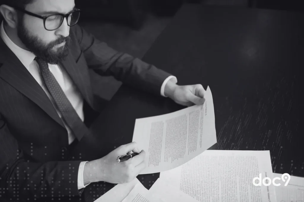 Homem analisando contrato em mesa de madeira escura com documentos e caneta, ilustrando um artigo da doc9 sobre parecer jurídico.